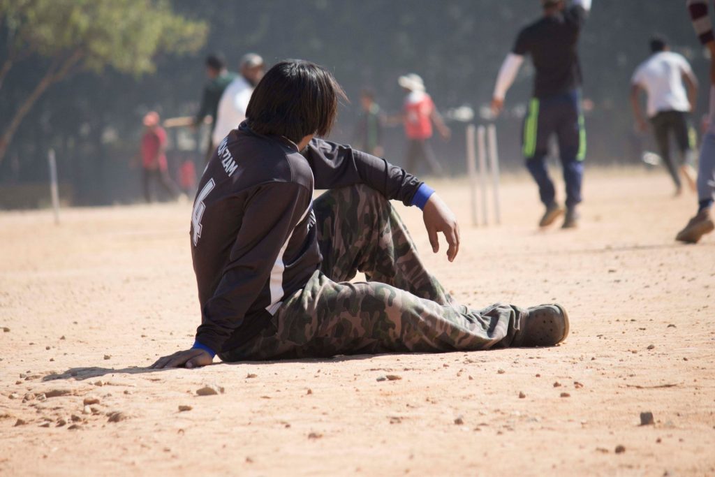Giovane giocatore di cricket seduto sul campo polveroso al sole