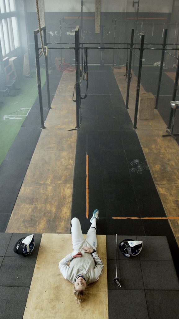 Atleta in tenuta da scherma distesa a terra in palestra, vista dall'alto