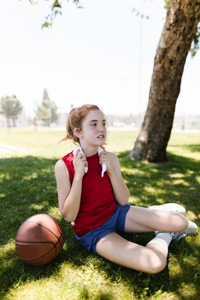Ragazza in tenuta sportiva seduta sull'erba con un pallone da basket