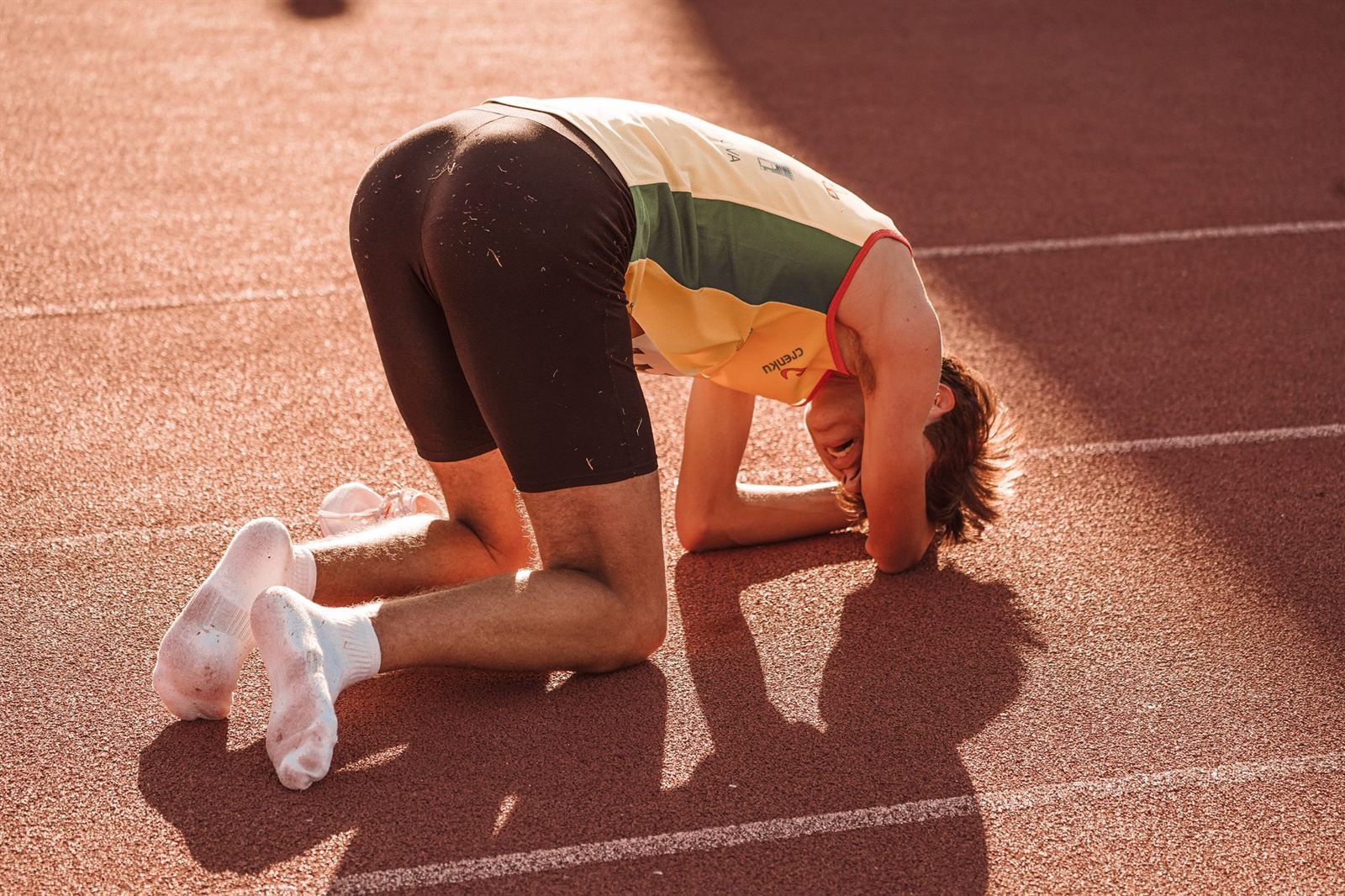 Corridore inginocchiato sulla pista, stremato dopo lo sforzo