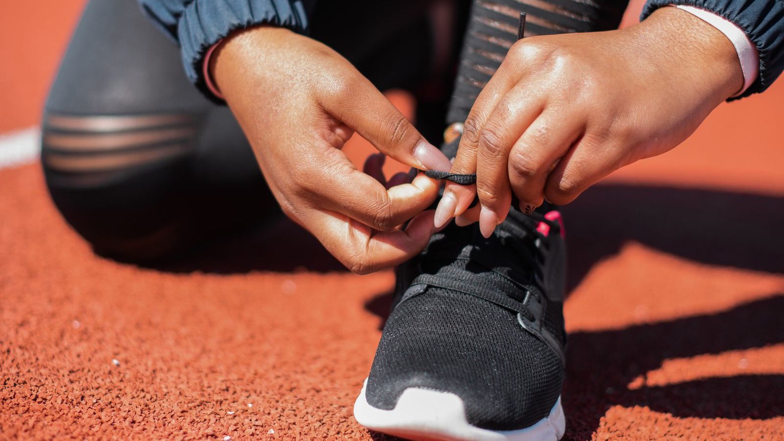 Primo piano di una persona che allaccia le scarpe da corsa su una pista di atletica